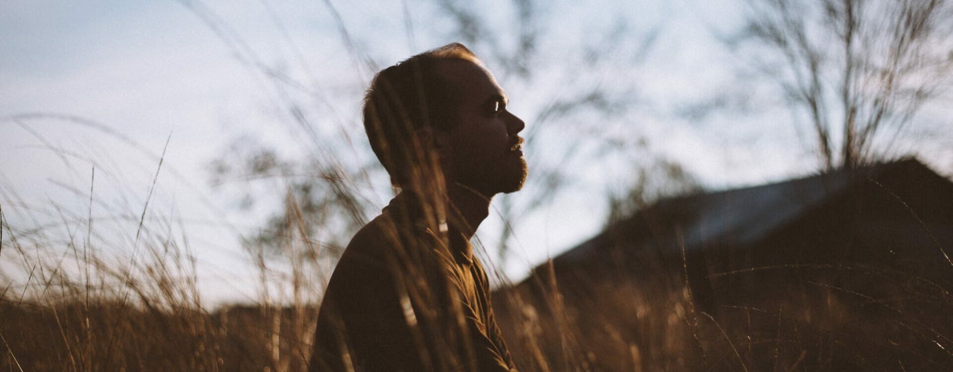 silhouette of man sitting on grass field at daytime